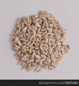 Top view of circle of shelled sunflower seeds against white vinyl background.