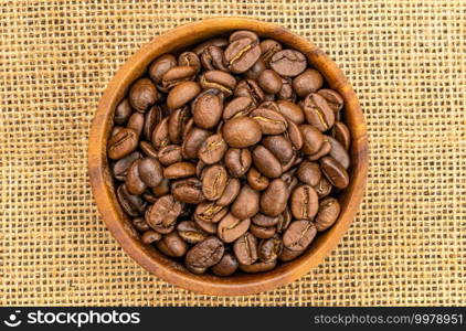 Top view of coffee beans in a wooden bowl on sackcloth. Roasted coffee beans in a wooden bowl.