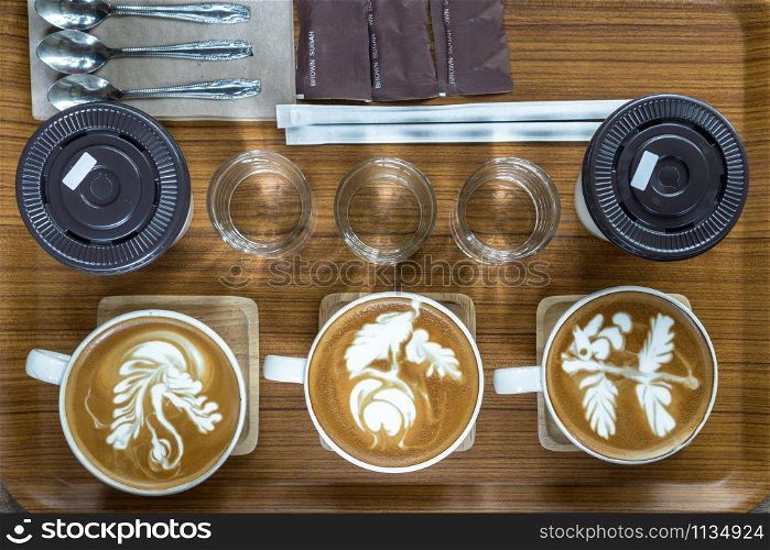 Top view of coffee cup set which consist of latte art, capuchino, glassed of water, spoon and sugar and ice coffee over the wooden plate and table, drink and coffee shop concept