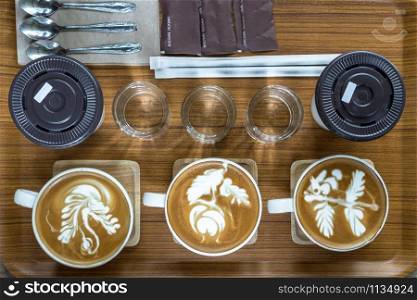 Top view of coffee cup set which consist of latte art, capuchino, glassed of water, spoon and sugar and ice coffee over the wooden plate and table, drink and coffee shop concept