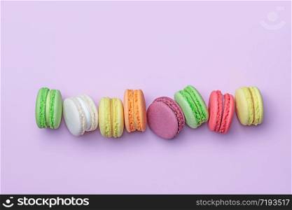 Top view of colorful macaron biscuits in a row on pastel color block background, flat lay