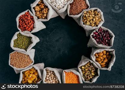 Top view of colorful nutritious cereals and dried fruit in small sacks standing in circle, isolated over dark background. Food concept