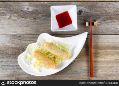 Top view of crispy spring rolls with dipping sauce and chopsticks in holder on rustic wooden boards.