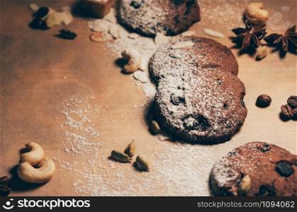 Top view of crunchy chocolate biscuits with nuts, cardamom and star anise on textured parchment backdrop, floured. Empty space for your text and design