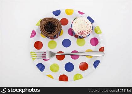 Top view of cupcakes in multicolored plate over white background