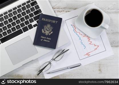 Top view of desktop with partial laptop, graph, coffee, reading glasses, pen and USA passport.