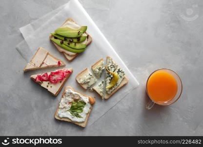 Top view of different kinds of sandwiches for tasting or having break isolated on table. Glass of orange juice not far from. Sandwiches with cheese, avocado, etc.. Different kinds of sandwiches