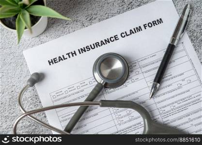 Top view of doctor stethoscope, pen and health insurance claim form on table