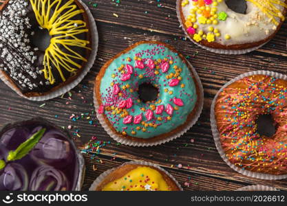 Top view of donuts in various colors and flavors on wooden table