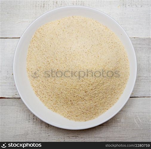 Top view of dry uncooked semolina in glass bowl on wooden background