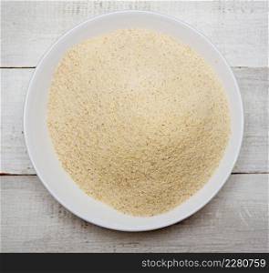 Top view of dry uncooked semolina in glass bowl on wooden background