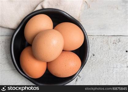 Top view of eggs in black bowl on wooden table.