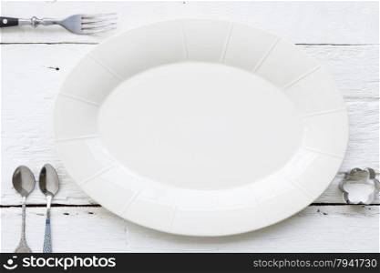 Top view of empty oval ceramic dish, fork, teaspoons and flower shape cookie cutter putting on white wooden table. retro, vintage and country style image