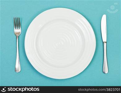 top view of empty white plate with fork and knife on green background