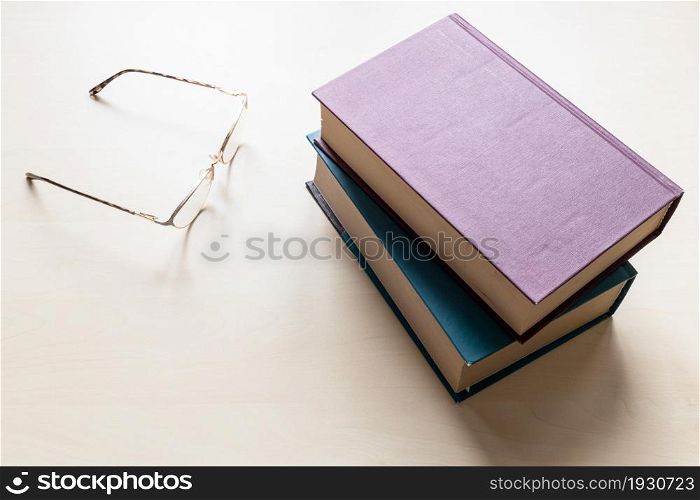 top view of eyeglasses and two blank books on light brown wooden board