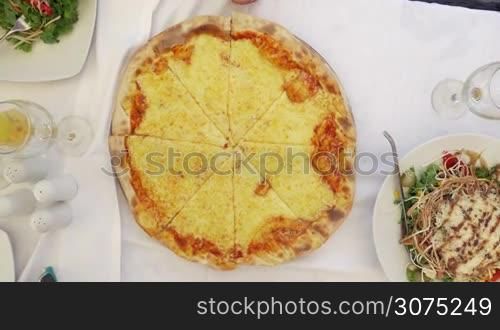 Top view of family taking slices of appetizing cheese pizza served in outdoor cafe