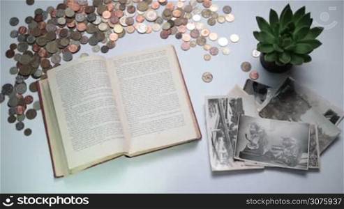 Top view of female hand turning pages of old book and vintage photos, coins on the white table