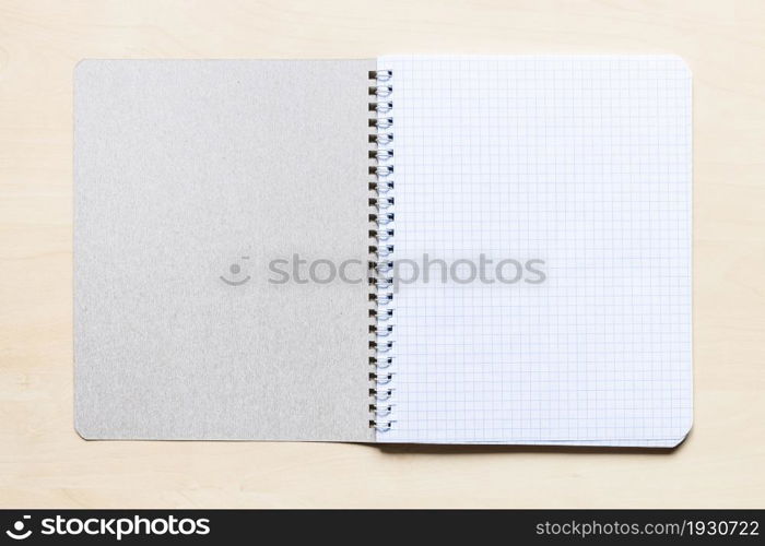 top view of first squared page of open blank spiral notebook on light brown wooden board