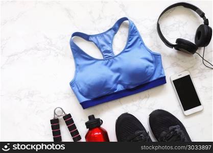 Top view of flat lay fitness equipment with sport bra, sneakers shoes, smartphone, earphones and bottle of water on white marble background. Top view of flat lay fitness equipment with sport bra, sneakers