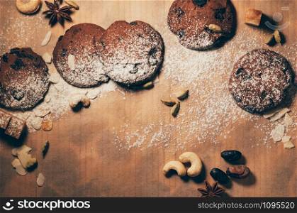 Top view of floured crunchy chocolate biscuits with nuts, cardamom and star anise on textured parchment backdrop. Empty space for your text and design
