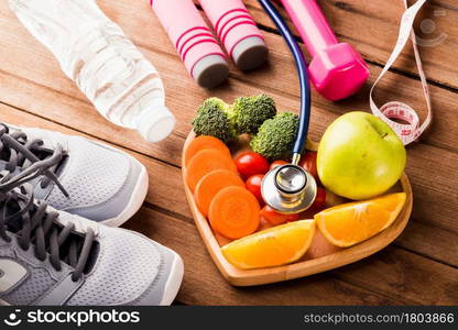 Top view of fresh fruits and vegetables in heart plate wood (apple, carrot, tomato, orange, broccoli) and sports equipment and doctor stethoscope on wooden table, Healthy lifestyle diet food concept