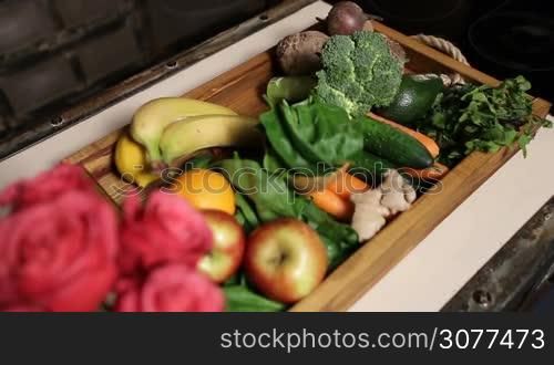 Top view of fresh fruits and vegetables in wooden tray on kitchen table closeup. Selective focus on bouquet of red roses. Top view closeup. Organic food for healthy lifestyle.