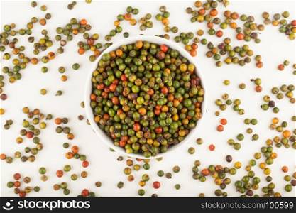 top view of fresh green and orange peppercorns in ceramic bowl on white background