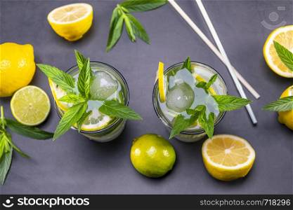 Top view of fresh lemonade with mint and ice in glasses on black background. Focus on leaf and ice.