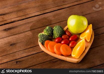 Top view of fresh organic fruits and vegetables in heart plate wood (apple, carrot, tomato, orange, broccoli) on wooden table, Healthy lifestyle diet food concept