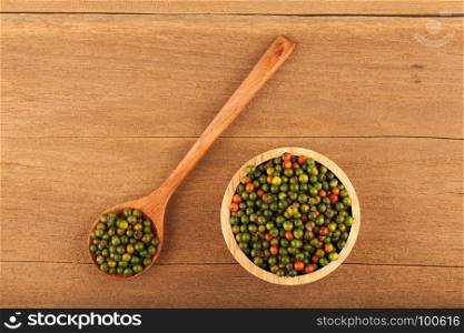 top view of fresh peppercorns in wooden bowl and spoon on wood background