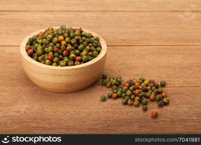 top view of fresh peppercorns in wooden bowl on wood background