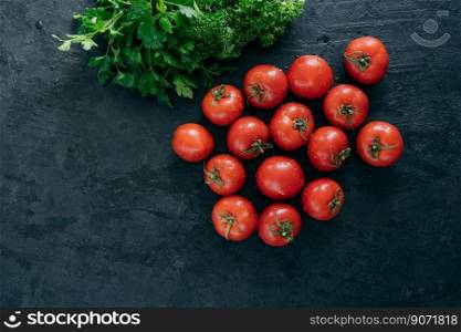 Top view of fresh red heirloom tomatoes and green parsley on black background. Vegetables containig vitamins. Vegeterian products.