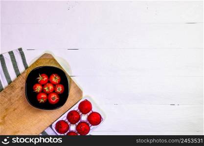 Top view of fresh ripe cherry tomatoes and red Easter eggs on a rustic white wooden table. Ingredients and food concept