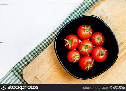 Top view of fresh ripe cherry tomatoes in small black bowl on a rustic white wooden table. Ingredients and food concept