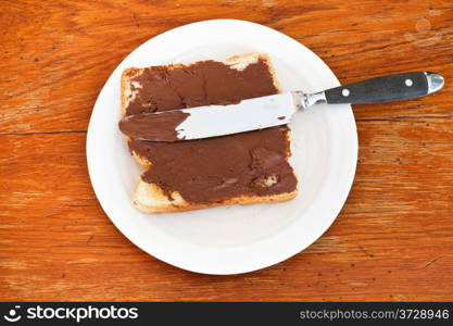 top view of fresh toast with chocolate spread on white plate, table knife on wooden table