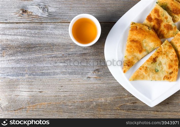 Top view of fried Asian pancakes, in white plate, with green tea on rustic wood. Plenty of copy space on left side