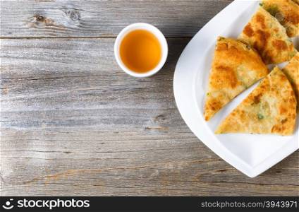 Top view of fried Asian pancakes, in white plate, with green tea on rustic wood. Plenty of copy space on left side