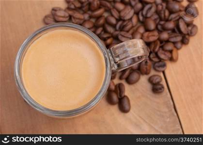 Top View of Glass Cup of Espresso Coffee on Wooden Table With Coffee Beans - Shallow Depth of Field