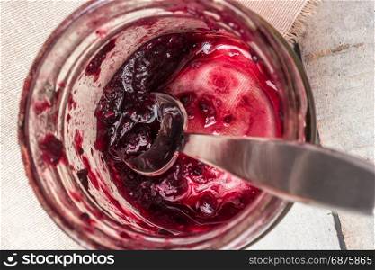 Top view of glass jar with red fruits jam and spoon.