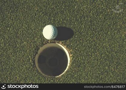 top view of golf ball on edge of course hole representing achivement and success business concept. top view of golf ball in the hole