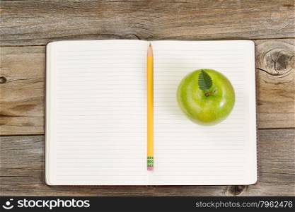 Top view of green apple, open notepad with pencil in center on rustic wood.