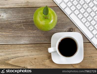 Top view of green apple, selective focus on top leaf and coffee, black coffee with partial computer keyboard on rustic wood.