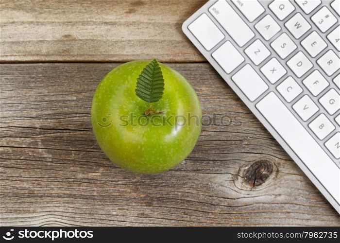 Top view of green apple, selective focus on top leaf, with partial computer keyboard on rustic wood.