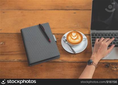 Top view of hand of woman using laptop computer with notebook and coffee cup. People and drinks and technology concept. Working woman theme.