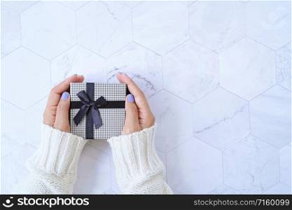 Top view of hands holding gift box from new year celebration or Christmas present on white marble background, holiday concept