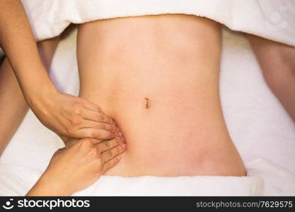 Top view of hands massaging female abdomen in a physiotherapy center. Therapist applying pressure on belly. Woman receiving a belly massage in a physiotherapy center.