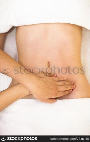 Top view of hands massaging female abdomen.Therapist applying pressure on belly. Woman receiving a belly massage at spa salon