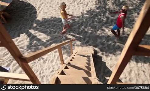 Top view of happy friends meeting on the beach and climbing up a wooden ladder on tree house to have a party