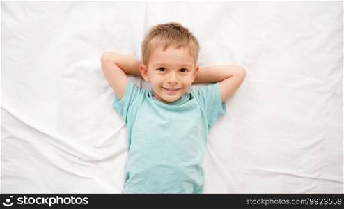 Top view of happy smiling toddler boy lying on bed and waving with hands like angel. Concept of happy children having good time at home.. Top view of happy smiling toddler boy lying on bed and waving with hands like angel. Concept of happy children having good time at home