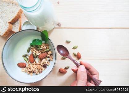 Top view of homemade yogurt with almond granola, fresh milk and whole wheat breads on wooden background with copy space